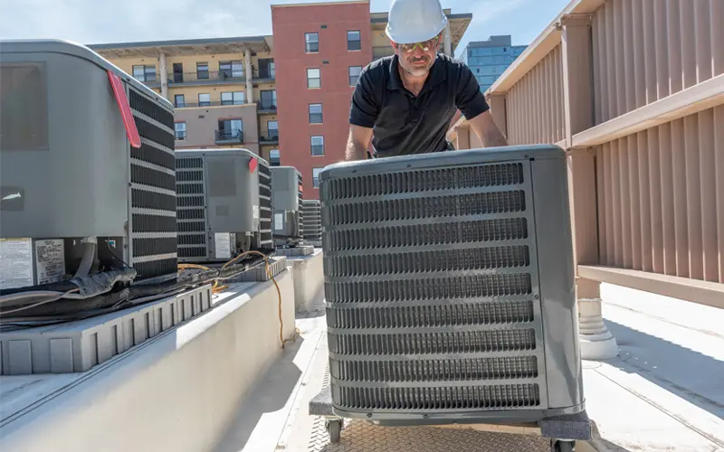 Air Conditioning Replacement Image 1_Reduced HVAC technician rolling in a new air conditioning unit on top of a building