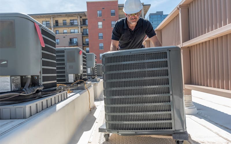 HVAC technician rolling in a new air conditioning unit on top of a building