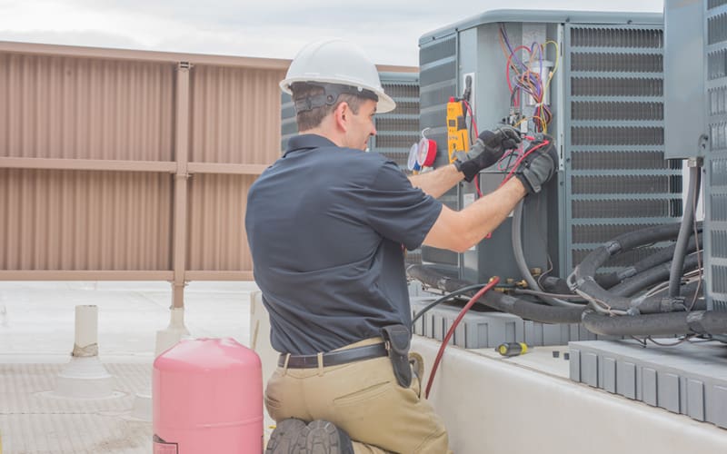 HVAC technician performing maintenance on an outdoor air conditioning unit